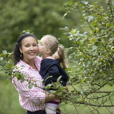 Ein Mädchen küsst ihre Mutter vor einem Apfelbaum auf die Wange.