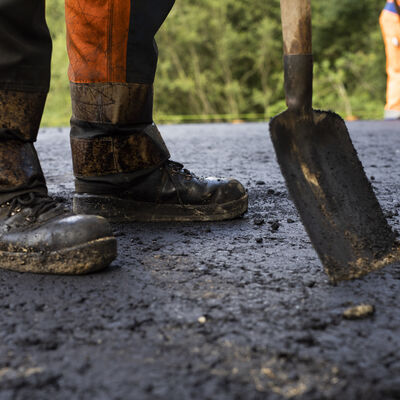 Baustelle: Stiefel und Schaufel auf frischem Asphalt.