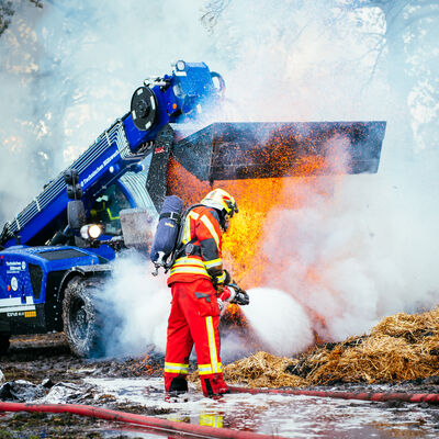 Feuerwehrmann löscht brennenden Heuhaufen. Das Technische Hilfswerk aus Kaltenkirchen unterstützt den Einsatz.