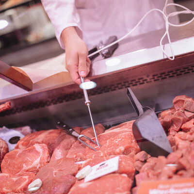 Ein Mitarbeiter steht an einer Fleischtheke und kontrolliert die Temperatur des Fleisches.