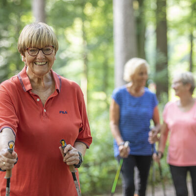 Seniorinnen beim Nordic Walking im Wald.