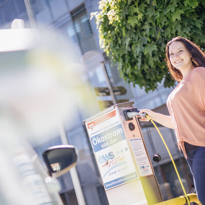 Eine junge Frau betankt ein Elektroauto vor dem Hauptgebäude des Kreises an einer Ladestation.