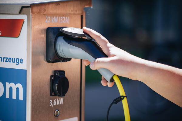 Eine Hand greift nach dem Aufladekabelstecker einer Ladestation für Elektroautos vor dem Hauptgebäude des Kreises.