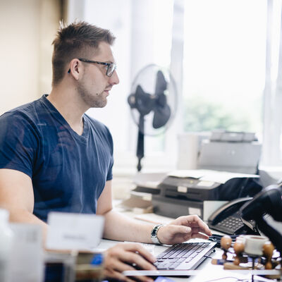 Ein Kreismitarbeiter arbeitet am Computer. Auf dem Schreibtisch stehen Telefon, Stempel und ein Drucker.