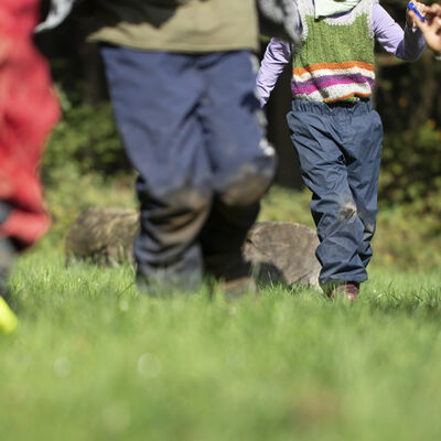 Kinder laufen in Matschhosen über eine Wiese.