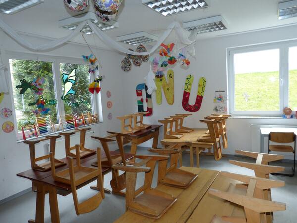 Klassenraum mit hochgestellten Stühlen. An der Wand hängen bunte Buchstaben.